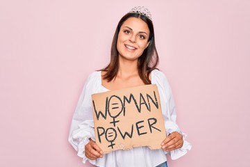 Girl wearing princess tiara asking for women rights holding banner with woman power message looking positive and happy standing and smiling with a confident smile showing teeth