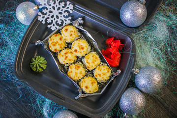 Baked rolls in a black container with ginger and wasabi with silver new year balls and artificial snowflake. Lunch in New Year's decoration