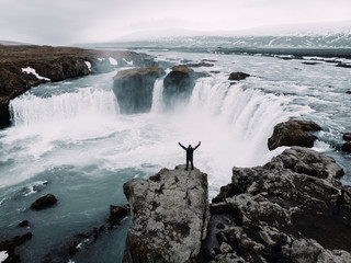 Man stands on the ledge of very famous Iceland waterfall Godafoss