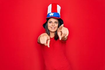 Young beautiful brunette woman wearing united states hat celebrating independence day pointing to you and the camera with fingers, smiling positive and cheerful