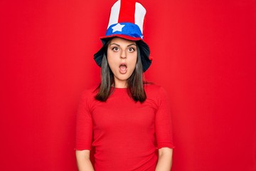 Young beautiful brunette woman wearing united states hat celebrating independence day afraid and shocked with surprise and amazed expression, fear and excited face.