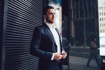 Businessman in classical suit with smartphone waiting in street in downtown