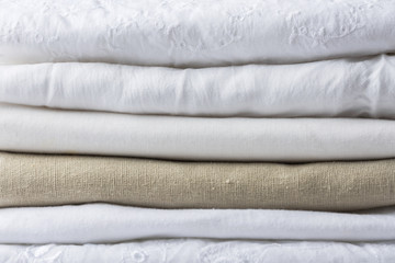 Stack of white and beige pure organic cotton and linen folded fabric. Clothing laundry home textile...