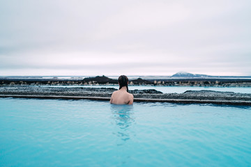 Young woman stands in blue lagoon watching the mountains in the background