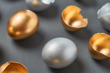 Golden and silver eggs, shells on dark concrete background. Concept of easter, pricelless ideas, successful business investment or luxury breakfast