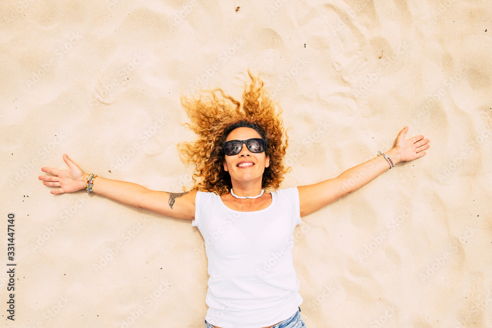 Wall mural happy and cheerful adult caucasian lady lay down on the sand at the beach enjoying freedom and healt