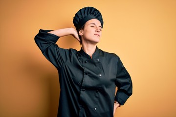 Young beautiful chef woman wearing cooker uniform and hat standing over yellow background Suffering of neck ache injury, touching neck with hand, muscular pain
