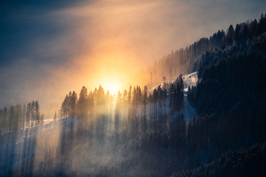 Goldenes Licht mit Sonnenstrahlen durch nebeliges Gebirge mit verschneiten Tannen. 