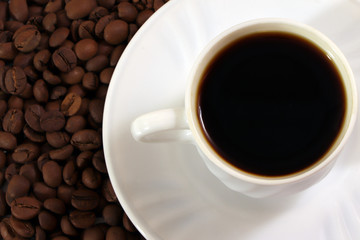 A white cup of coffee and coffee beans on a wooden table.