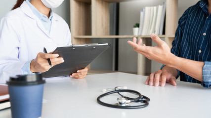 doctor working with patient taking notes with clipboard and discussing something in his medical office, health care and people concept