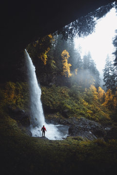 Massiver Wasserfall &uuml;ber Kante St&uuml;rzend in Becken umrundet von kanadischen Tannen und herbstlaub im Vordergrund sowie kleiner Person im Vordergrund 