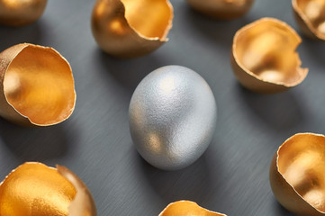 Silver egg and gold shells on dark concrete background. Concept of easter, pricelless ideas, successful business investment or luxury breakfast