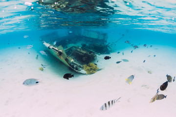 Ocean with wreck of boat on sandy bottom and tropical fish underwater in Mauritius