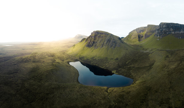 Gr&uuml;ne H&uuml;gellanschaft mit goldenem Sonnenaufgang und See im Vordergrund. Schottisches Hochland. 