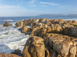 Fototapeta na wymiar Sunlight rocks in sea foam with sea, sky and landscape in the background.