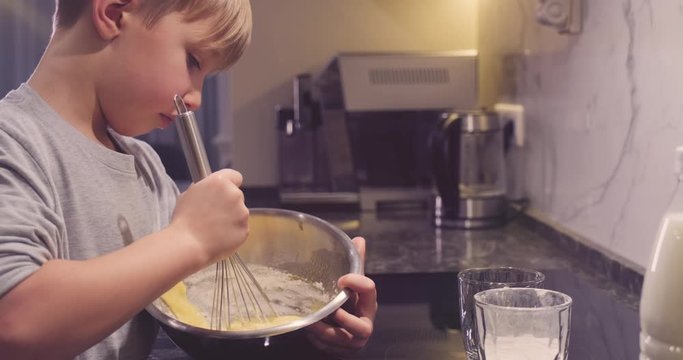 Сhild whips the pancake mixture with a whisk in an iron bowl.  8-year-old boy cooks in the kitchen.