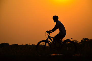 Obraz na płótnie Canvas Silhouette men riding bicycles at sunset with orange sky in the countryside