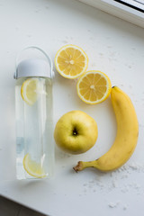 Water and yellow fruits on a white background. Lemon, banana, apple. Healthy food.