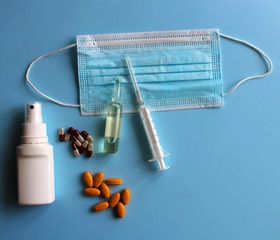 Medical mask with ampoule, syringe, antiseptic, medicines on a blue background. Covid19, coronavirus and epidemic content. Virus prevention and creating a vaccine against coronavirus. Copy space