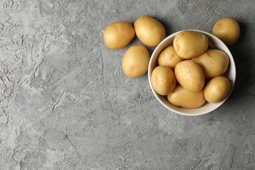 Bowl with young potato on grey background, top view