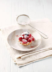  Little mascarpone tart with fresh raspberries on wooden background.