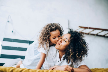 Cute baby kissing mother on bed