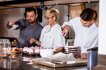 Group of workers in uniform decorating desserts in modern manufacturing.