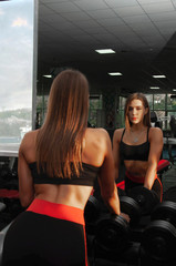 Front view of athletic pretty girl in sport crop top lifting weight in gym. Attractive young woman...