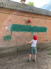 The concept: the game of ball, sports, leisure, child. A boy plays basketball on the street alone against a brick wall.