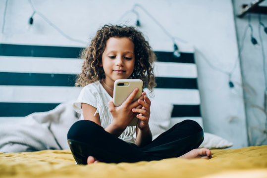 Content girl sitting with smartphone on bed