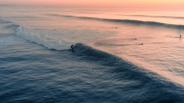 Beautiful aerial view of a profesional surfer surfing a perfect wave on a sunset / sunrise. Amazing ocean swell, foam. Top travel destination and extreme sport. Summer time.