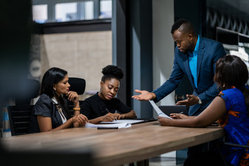 African businessman talking with a diverse group of female colleagues while having a meeting...