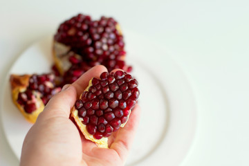   Juicy opened pomegranate in a hand on a white background. Eco healthy food. Grains of natural pomegranate.