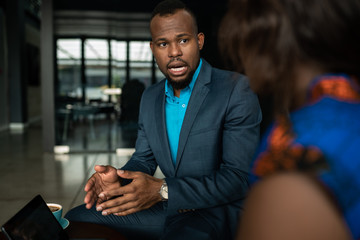 Black African businessman discussing work on a digital tablet during a casual meeting together over coffee in an office