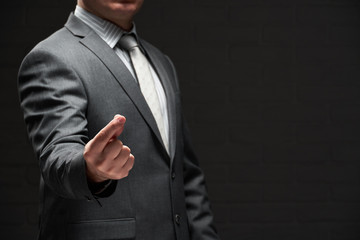 businessman demonstrating something in his fingers, dressed in gray suit, dark wall background