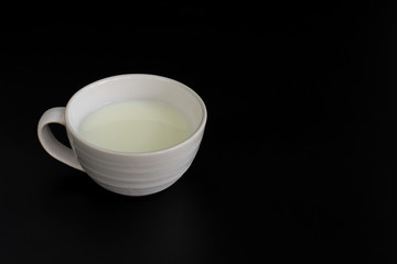 Side view of white cup of milk on black background with copy space. High protein and calcium. Healty beverage.