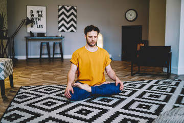 Young man doing basic yoga exercise in contemporary living room