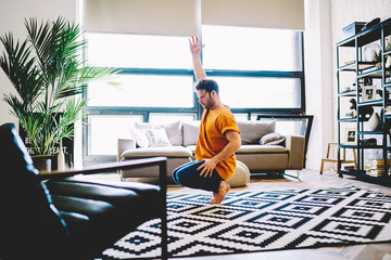 Young man sitting on tiptoes and practicing yoga pose in modern living room