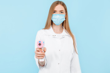 A female doctor in a protective mask measures the temperature using a non-contact infrared...