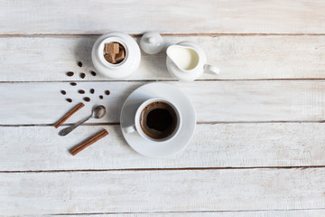 cup of black coffee, milk, sugar, coffee beans, cinnamon sticks, spoon on wooden background