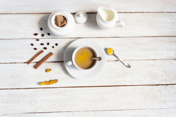 Cup of coffee with milk, turmeric powder, sugar on white wooden background