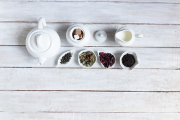 Tea time with teapot, milk, sugar, leaves of black, green, herbal, red tea on white wooden...