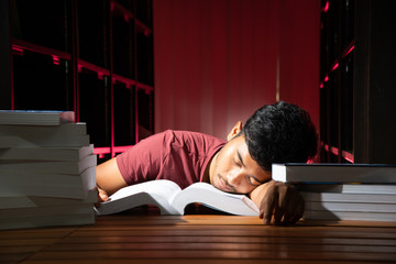 Fototapeta premium Portrait of black Thai Asian handsome guy wear dark red shirt working tried and burnout sleeping on book looking straight with a lot of book in dark red library stock photo
