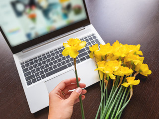 Bouquet of Narcissus or daffodils lying on silver metal laptop. Bright yellow flowers on portable...