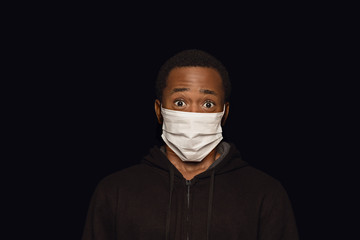Shocked man in protective mask on black background. Prevention against pneumonia, keep on being on quarantine, staying home. Chinese coronavirus treatment. Healthcare, medicine, isolation concept.