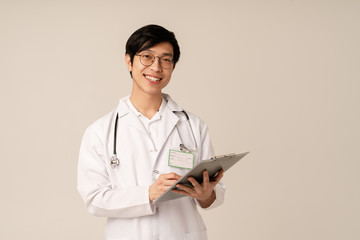 Image of asian young doctor in uniform taking notes on clipboard