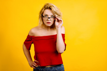emotional girl posing on a yellow background. blonde in a red top. young woman in glasses is surprised