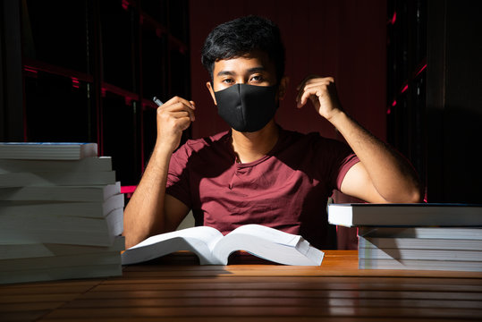 Portrait of black Thai Asian handsome guy vintage hair style wear black mask and dark red shirt sitting still with a lot of book in dark red library stock photo
