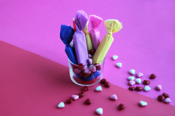 Candies wrapped in colored papers in glass on double pink surface,close up 