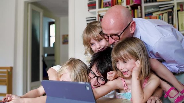 Three little sisters indoor at home using tablet sitting table supervised by parents - education, security, streaming concept